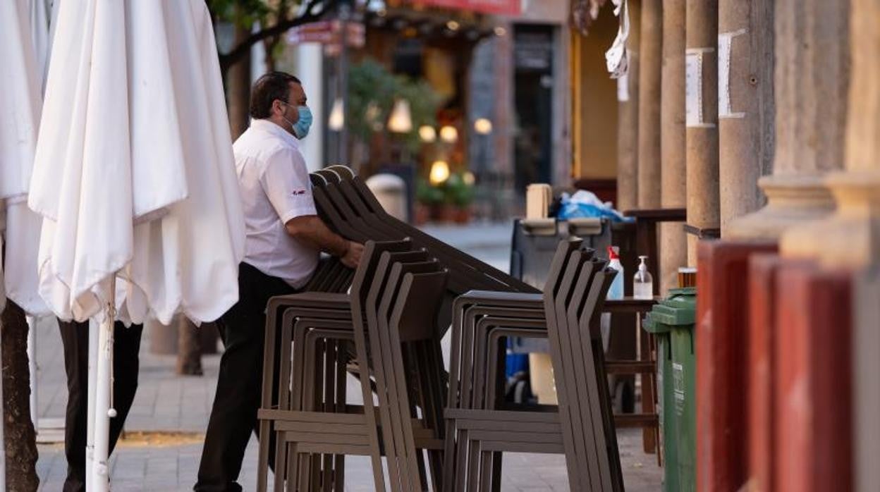 Un camarero recoge las sillas de la terraza de un establecimiento sevillano