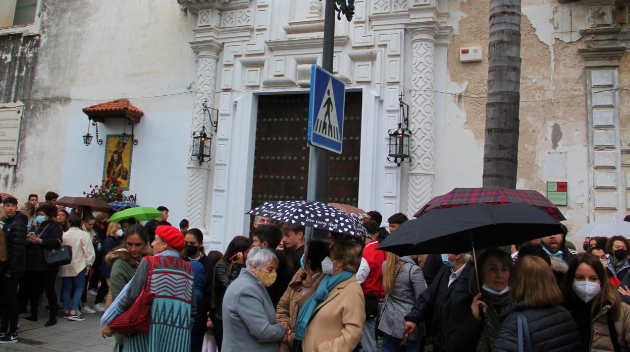 Muchas personas esperando con el paraguas en la mano frente a la Capilla del Hospital San Juan de Dios.