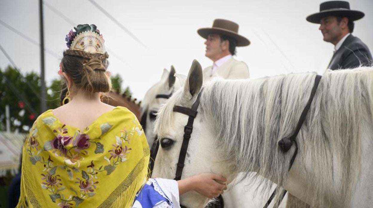 Una mujer vestida de flamenca acaricia a un caballo en el real de la Feria