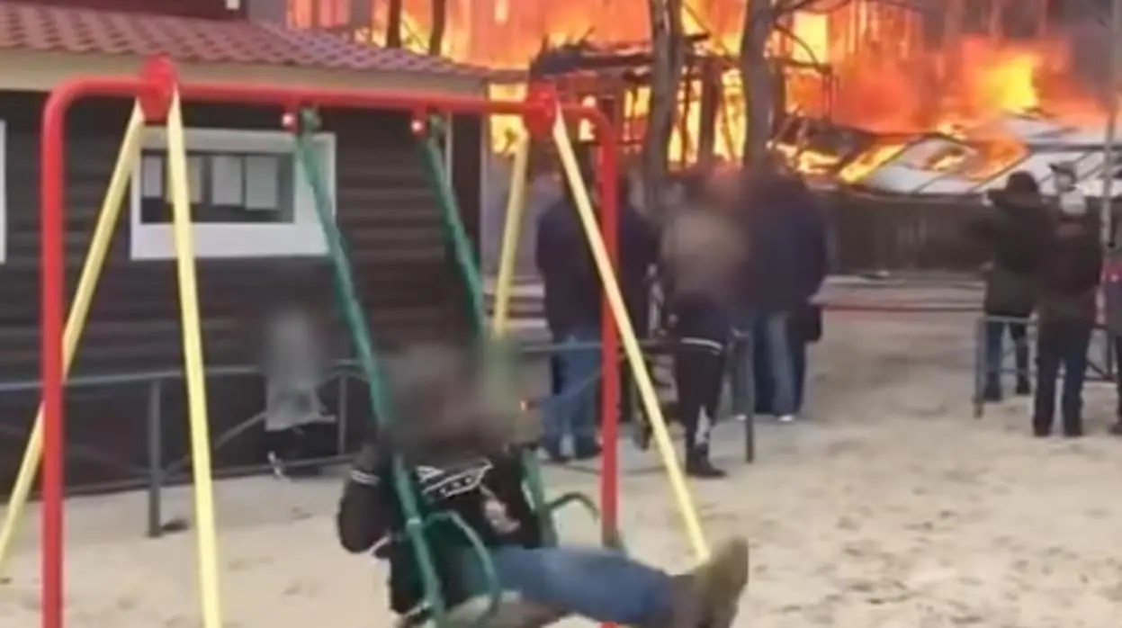 Un niño se columpia tranquilamente delante de un incendio