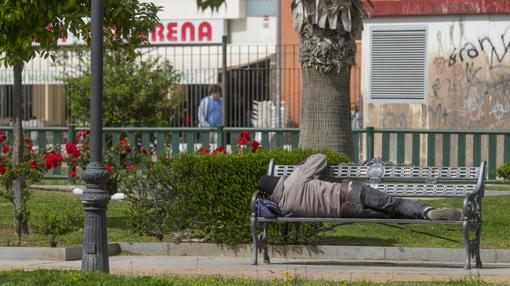 Un indigente reposa en un banco del parque de los Perdigones