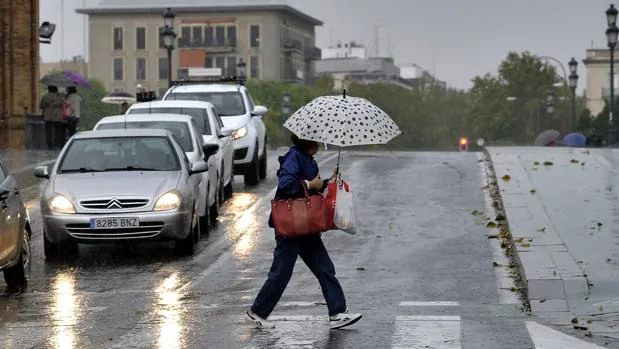 Una mujer se protege de la lluvia con un paraguas en el puente de Triana