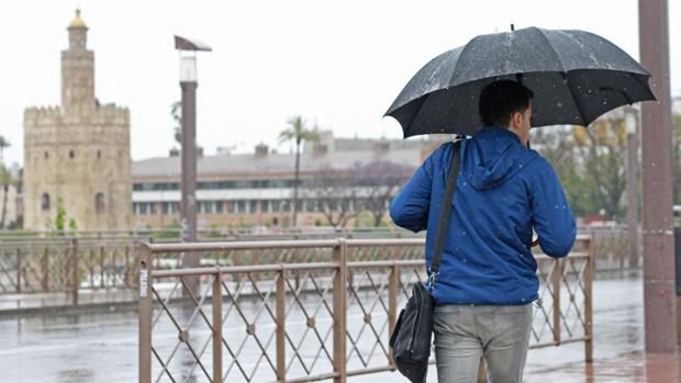 Un joven se resguarda de la lluvia bajo un paraguas en Sevilla