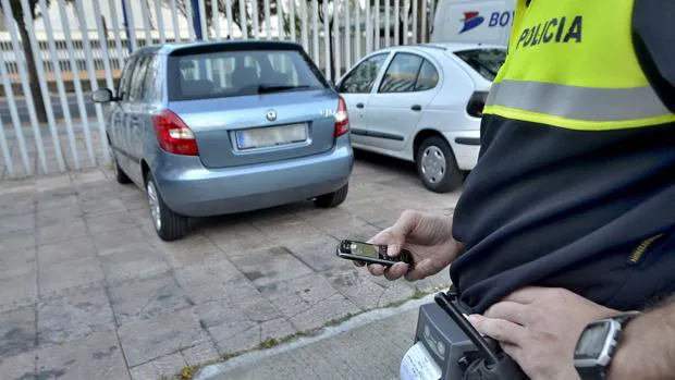 Un policía municipal pone una multa a un vehículo mal estacionado con su dispositivo móvil