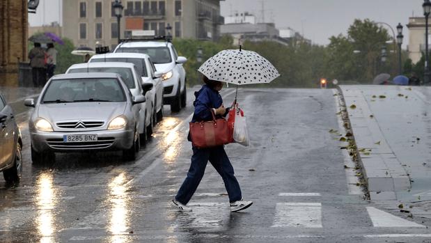 Una señora se refugia de la lluvia con su paraguas en Sevilla