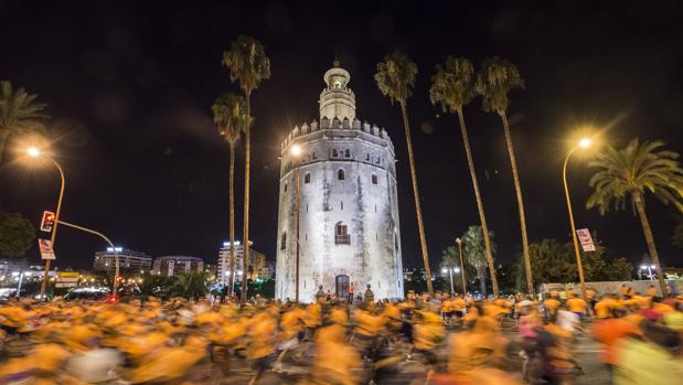 Corredores de la carrera nocturna del Guadalquivir pasan por delante de la Torre del Oro