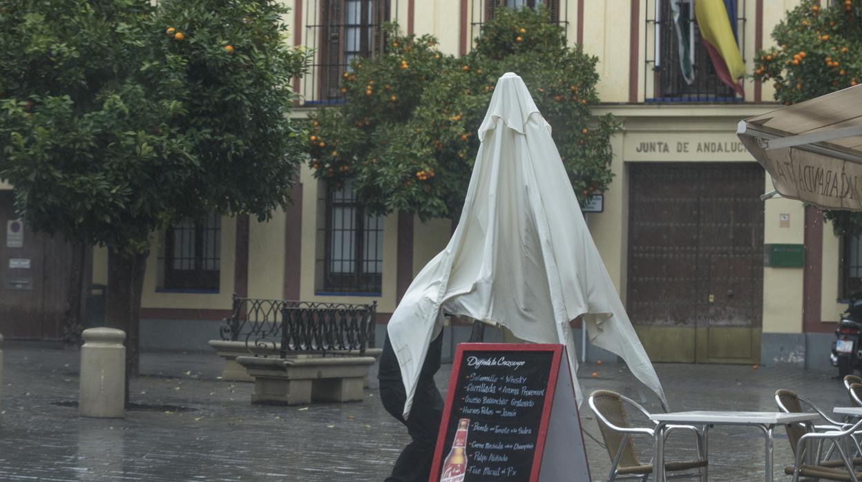 Una persona se refugia de la lluvia en la sombrilla en Sevilla