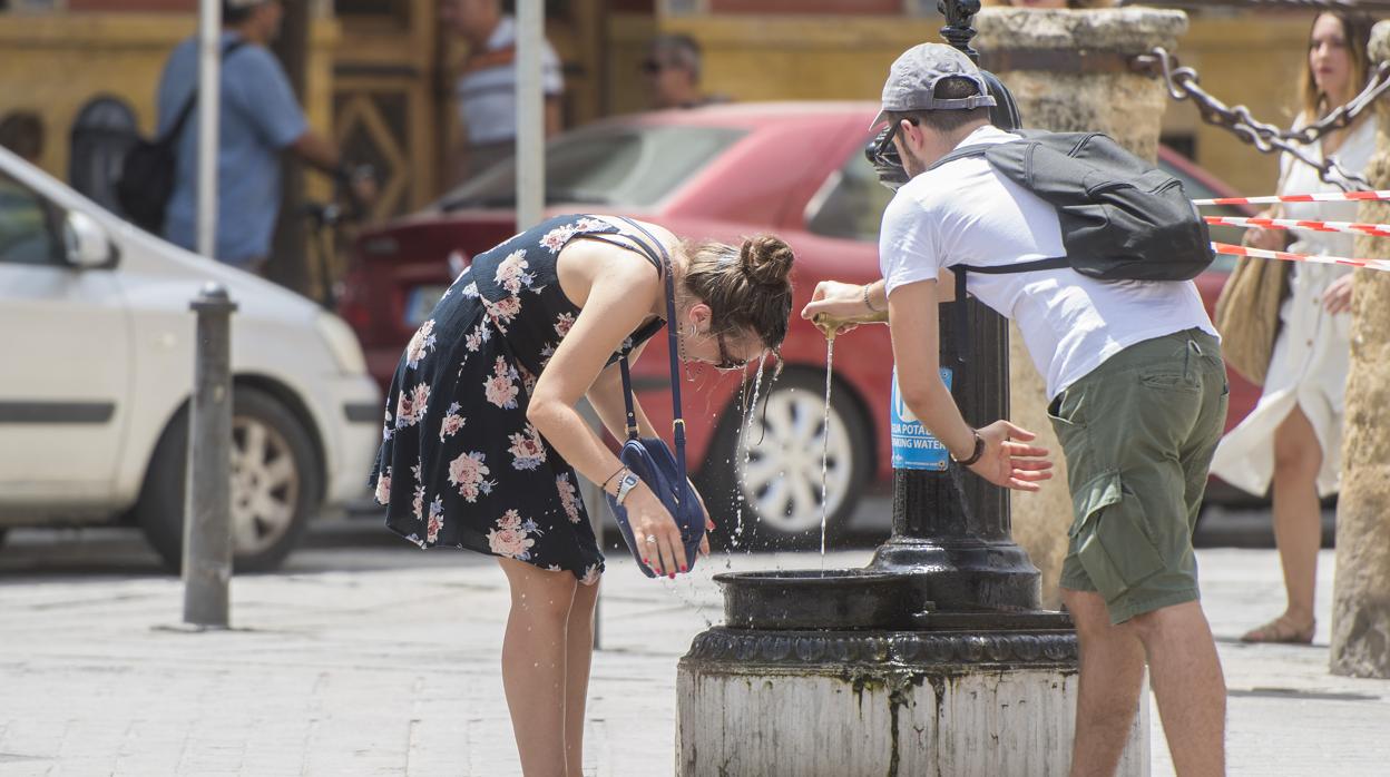 Unos turistas se resfrescan en una fuente en el centro de Sevilla