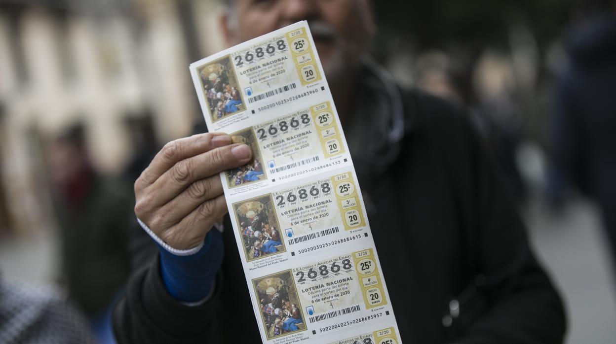 Una hombre enseña una tira de boletos de la lotería del Niño en Sevilla