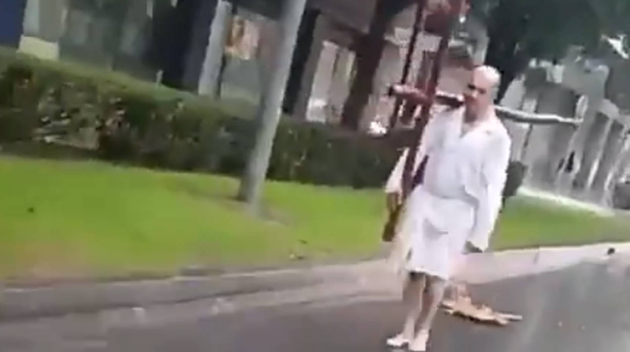 El hombre protagonista del vídeo, camina con una cruz al hombro bajo la lluvia en Sevilla