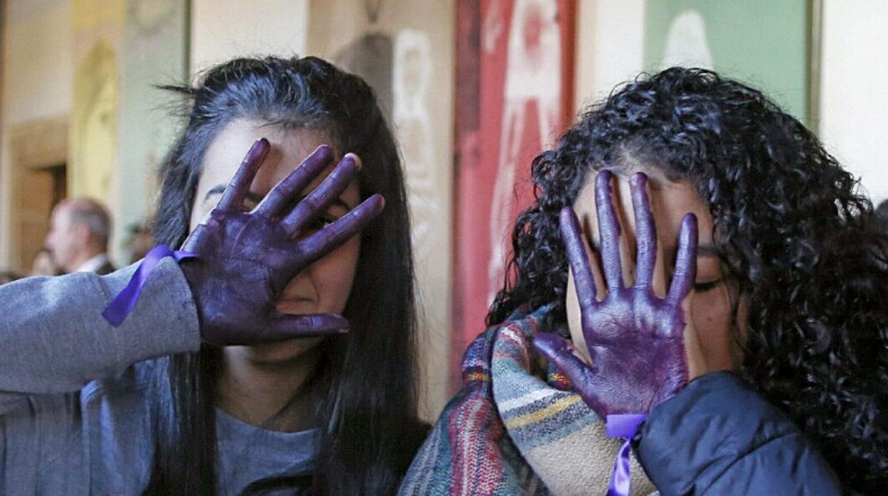 Dos jóvenes tapan su cara con las manos pintadas de morado como muestra de repulsa a la violencia de género