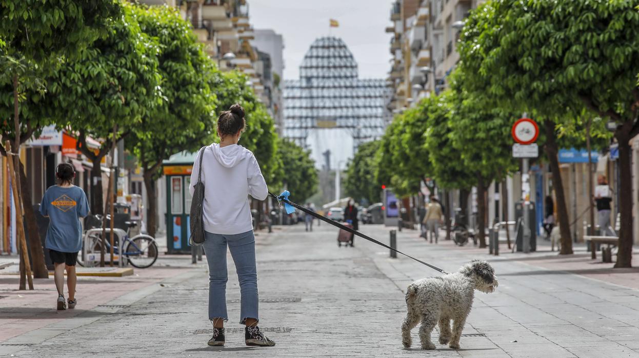 Una joven pasea al perro por la calle Asunción con la portada de la Feria sin terminar