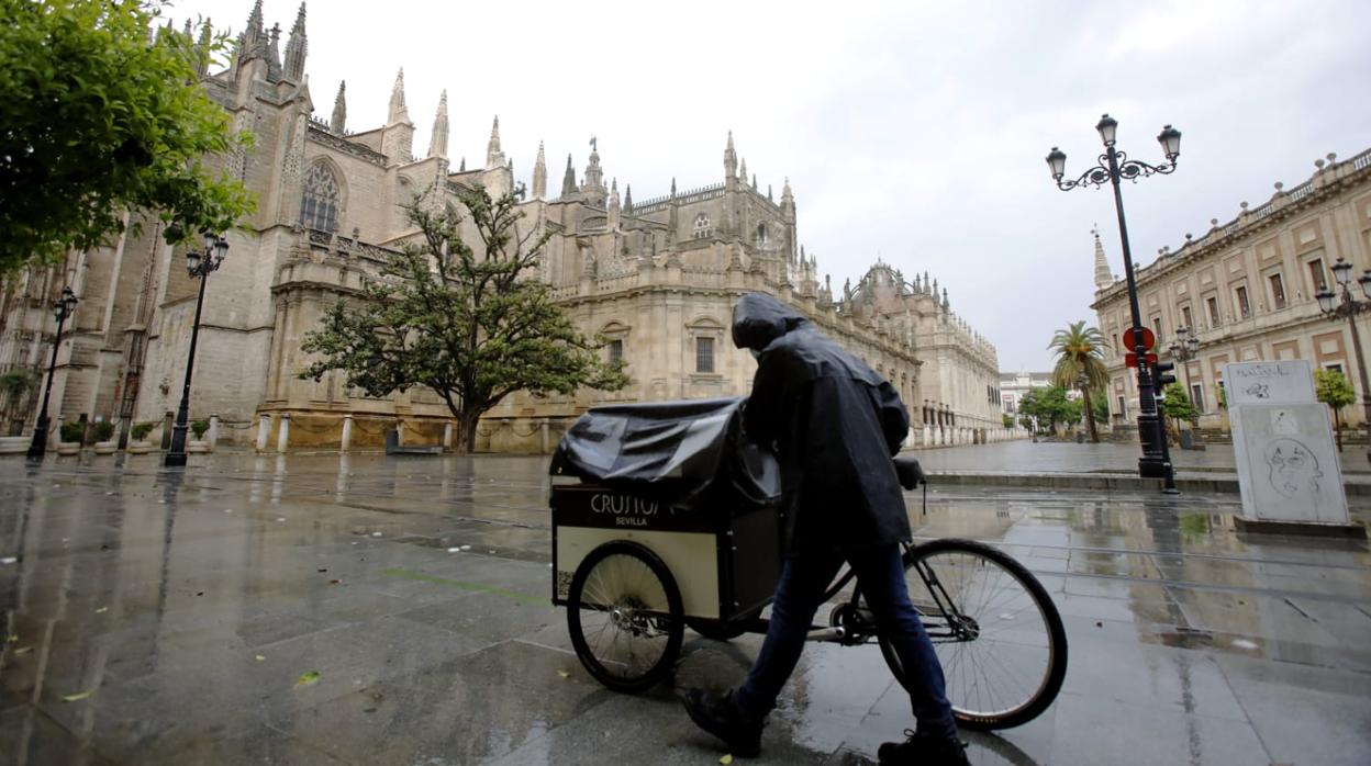 Una persona traslada un carro bajo la lluvia al lado de la catedral de Sevilla