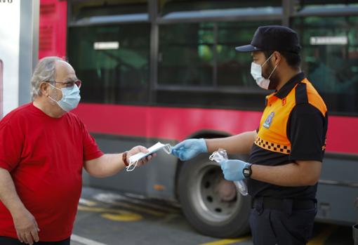 Un voluntario de Protección Civil entrega una mascarilla a un viajero