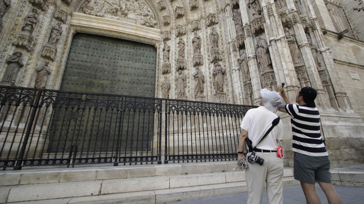 Dos turistas fotografían la puerta de la Asunción de la Catedral de Sevilla