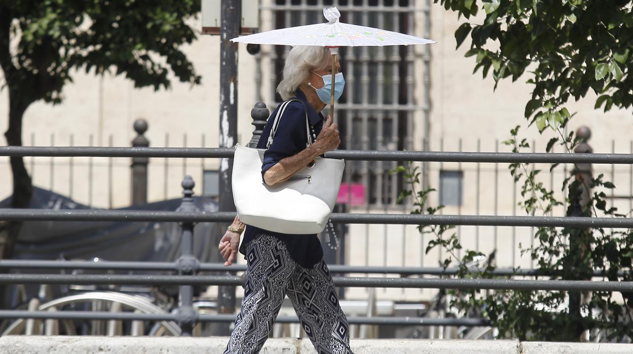 Una señora pasea por la calle protegida con una mascarilla a pesar del fuerte calor