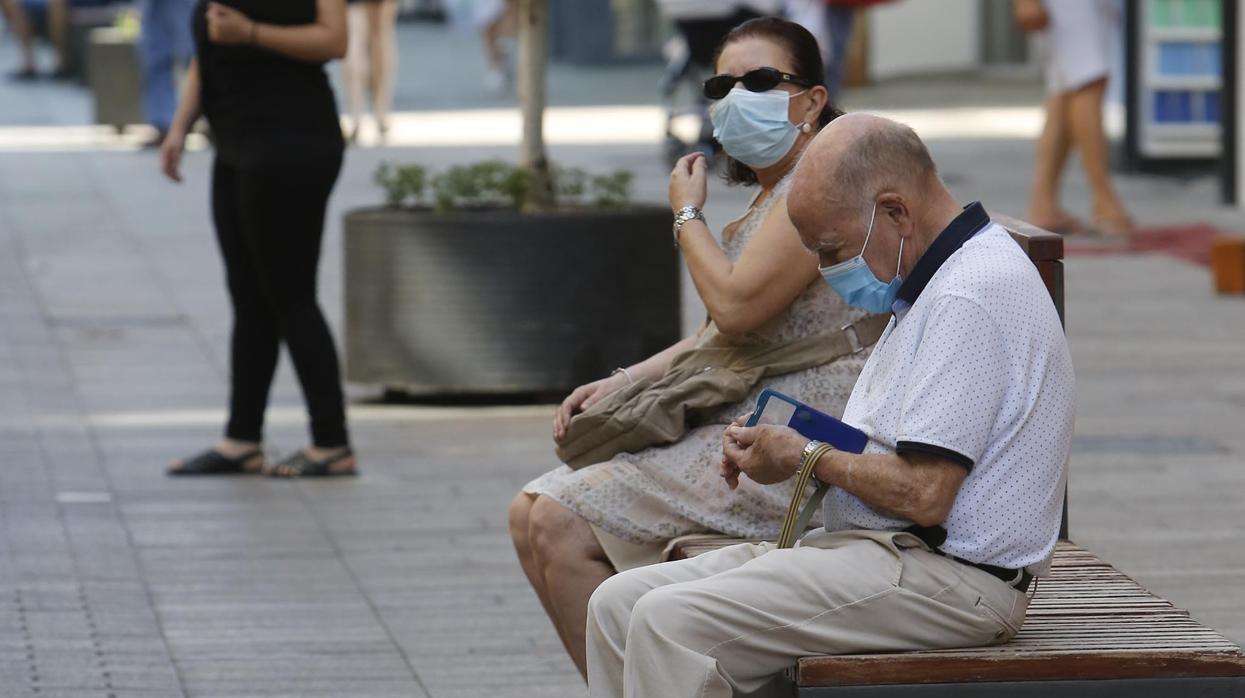 Dos personas sentadas con sus respectivas mascarillas en un banco