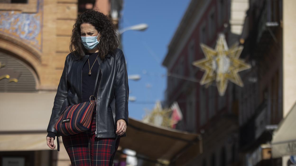 Una mujer con mascarilla camina por la plaza de San Francisco y al fondo, las luces del alumbrado de la calle Sierpes