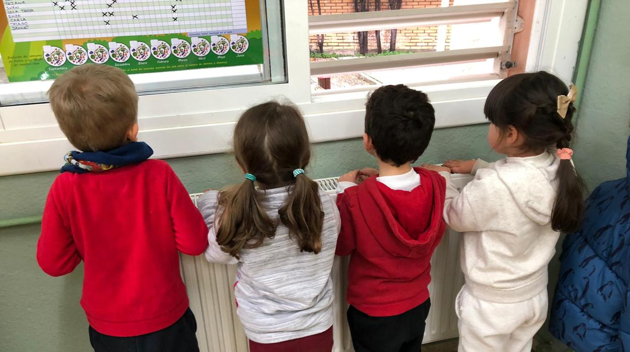 Sobre estas lineas cuatro niños se calientan en un radiador de una clase en Sevilla