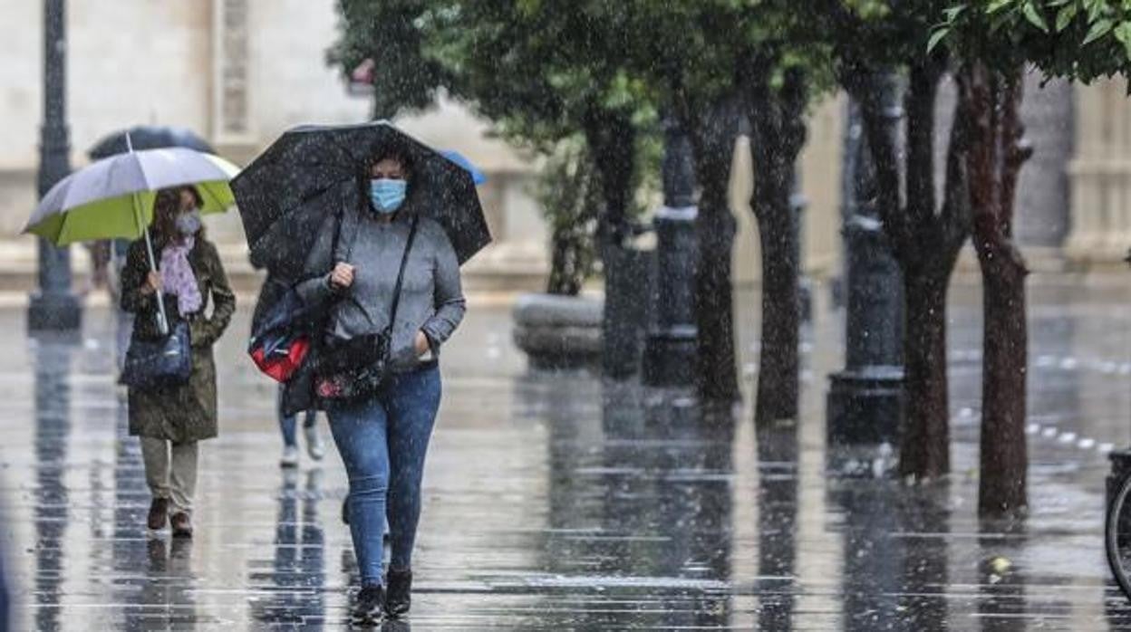 Varias personas pasean por Sevilla bajo la lluvia