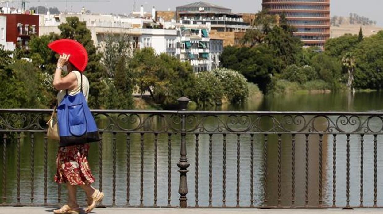 Una mujer se protege del sol con un abanico mientras cruza el Puente de Isabel II