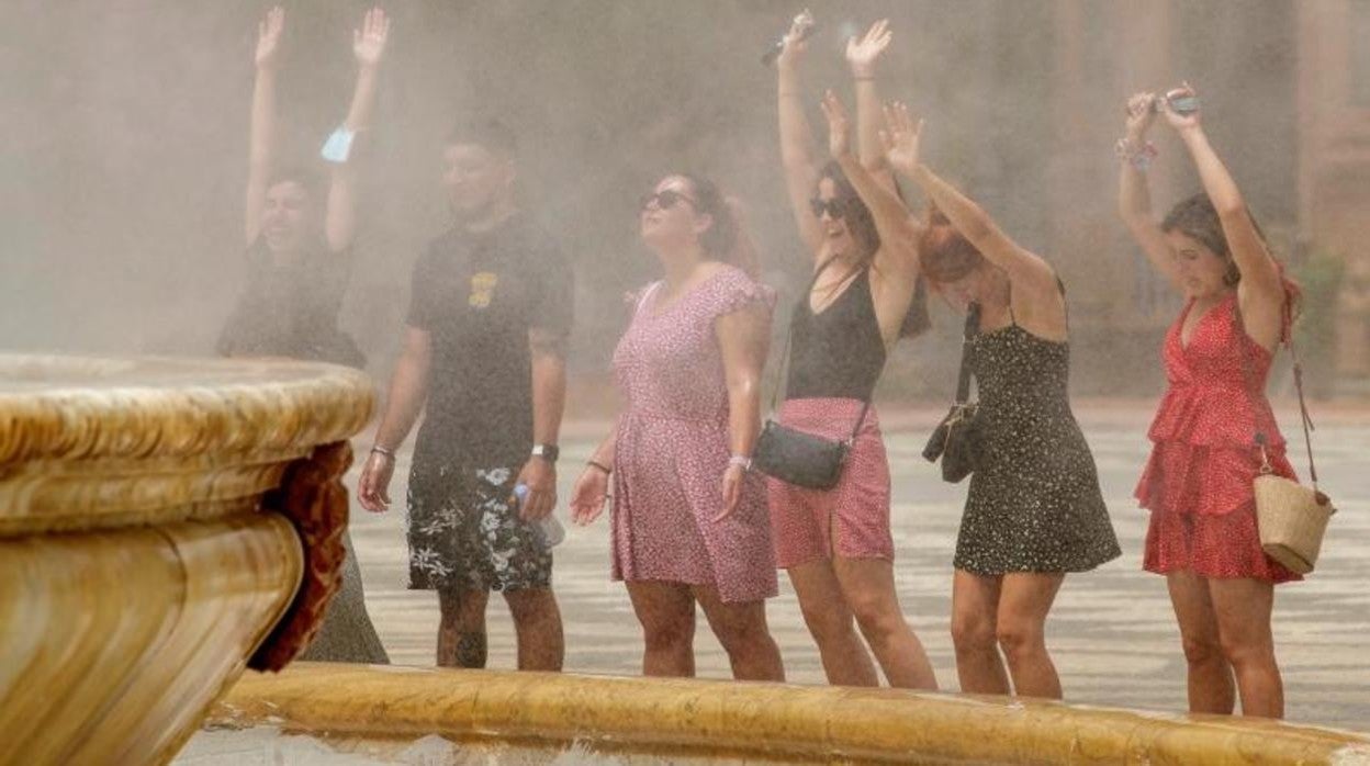 Varias personas se refrescan en la fuente de la Plaza de España de Sevilla