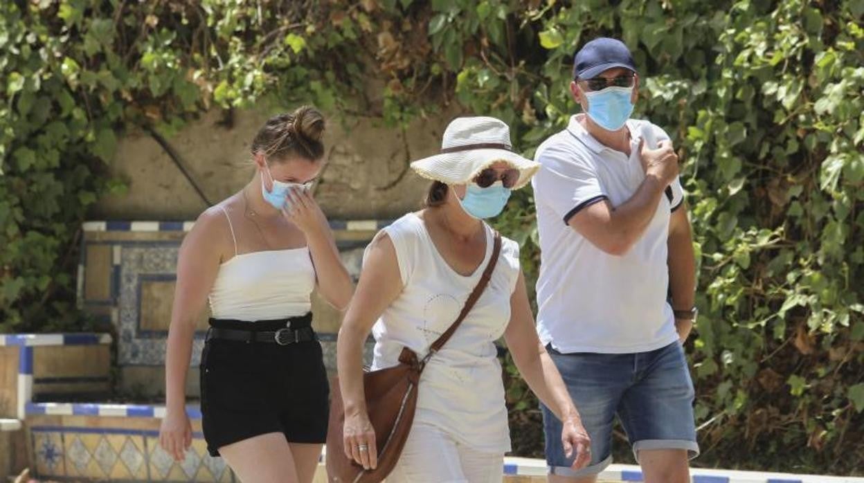 Tres personas pasean por Sevilla intentando protegerse del calor yendo por la sombra