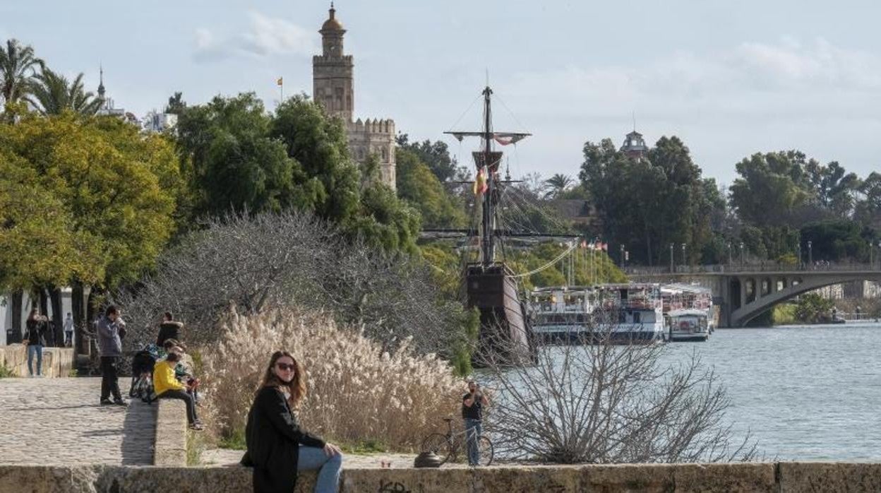 Una mujer descansa al borde del río Guadalquivir con la Torre del Oro de fondo