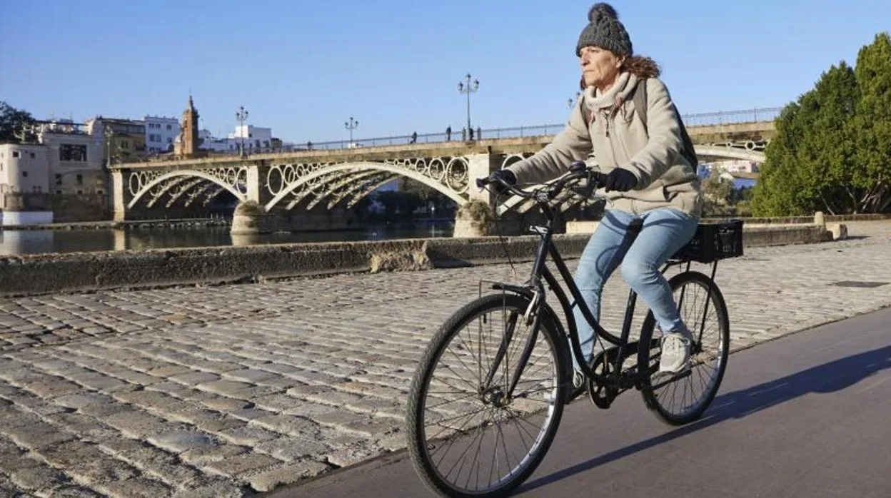 Una mujer se desplaza en bicicleta por la orilla de Sevilla del río Guadalquivir