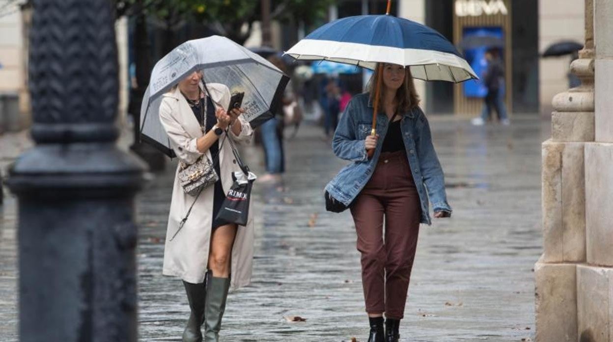 Dos mujeres pasean por Sevilla protegidas con paraguas por la lluvia