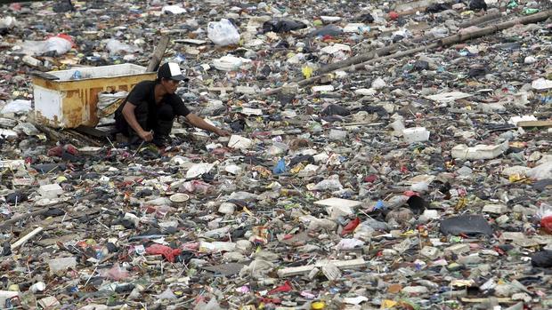 Un hombre recoge plásticos entre la basura que flota en uno de los ríos contaminados de Yakarta (Indonesia)