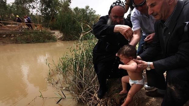 Un sacerdote ortodoxo bautiza a un niño en el río Jordán