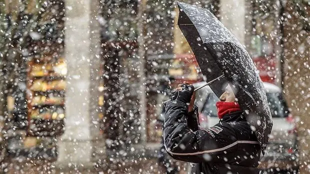 Un hombre toma una fotografía en una céntrica calle de la capital burgalesa que hoy amanecía bajo una intensa nevada