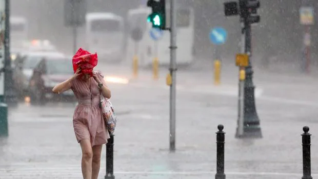 Una mujer pugna con la lluvia, de la que trata de guarecerse como le es posible