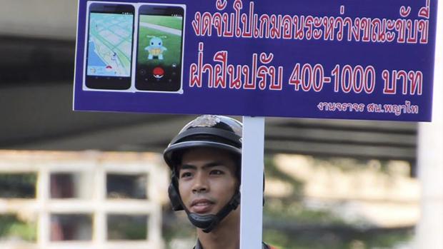 Un guardia de tráfico sostiene una pancarta en la que se lee «No juege a Pokemon Go mientras conduce, los infractores serán multados» durante una campaña contra el uso del videojuego en una concurrida calle de Bangkok, Tailandia