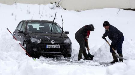 Dos personas retiran la nieve acumulada en su vehículo y despejan la estrada a su casa en la localidad navarra de Espinal