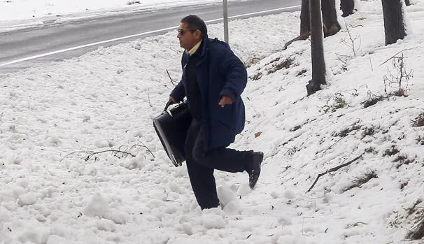 Un hombre cargado con una maleta trata de cruzar una cuneta cubierta de nieve a causa de la intensa nevada sufrida en la zona