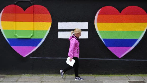 Una mujer camina junto a una pintada de dos corazones con los colores del arcoíris en Dublín
