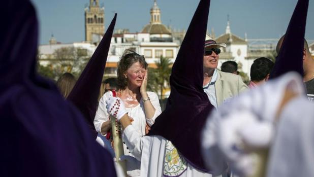 Unos turistas se protegen del sol con crema al paso de los nazarenos de la Hermandad de La Estrella, en el puente de Triana en Sevilla, ayer Domingo de Ramos