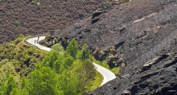 Unos ciclistas circulan junto a una ladera calcinada por un incendio forestal registrado en Quiroga (Lugo)