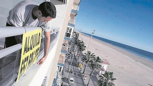 Un gaditano coloca el cartel de arrendamiento de su vivienda a pie de la Playa Victoria