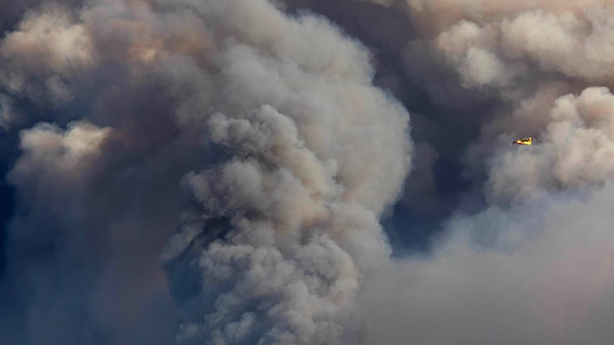 Un avión vuela a través de una columna de humo producto de un incendio forestal en Vila do Rei