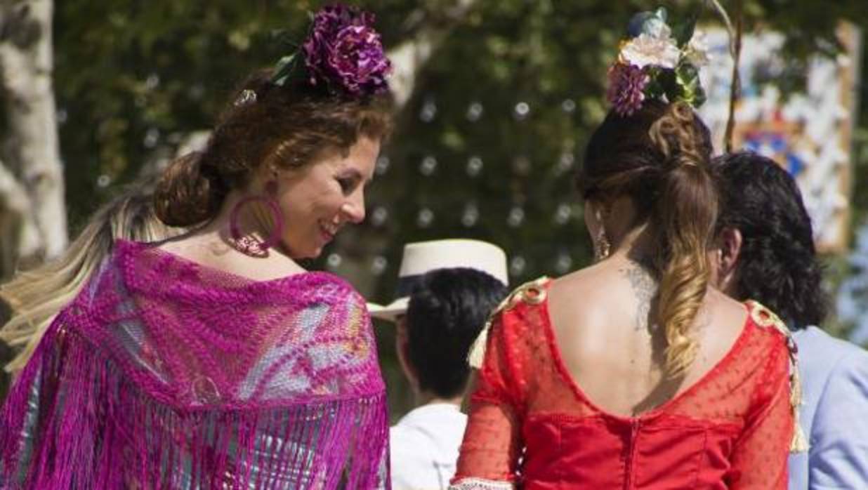 Dos chicas se pasean en coche de caballos por el Real de la Feria de Abril de Sevilla en una jornada en la que el calor es el protagonista