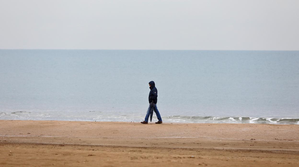 Un hombre pasea abrigado por la playa