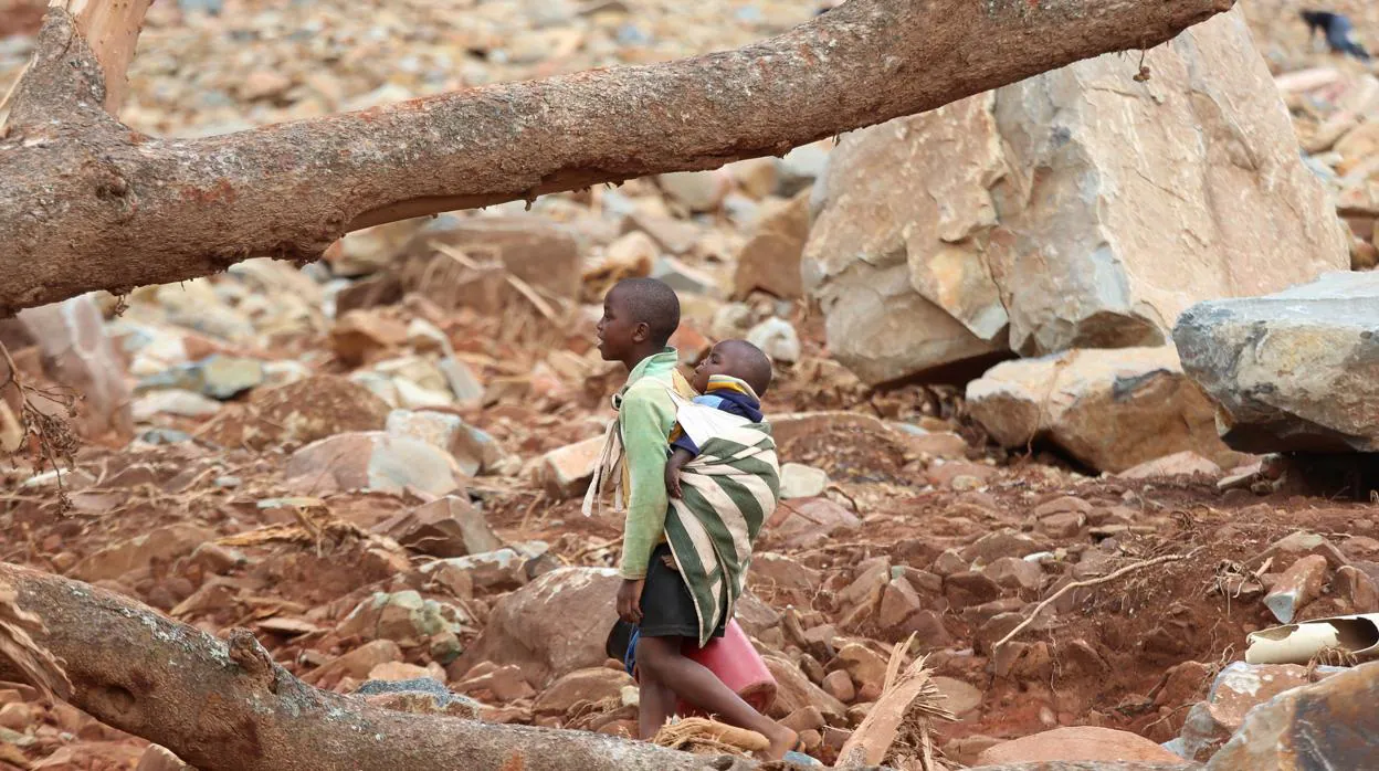 Un niño con un bebé en su espalda camina a través de escombros después del ciclón Idai en Ngangu, Chimanimani, Zimbabue