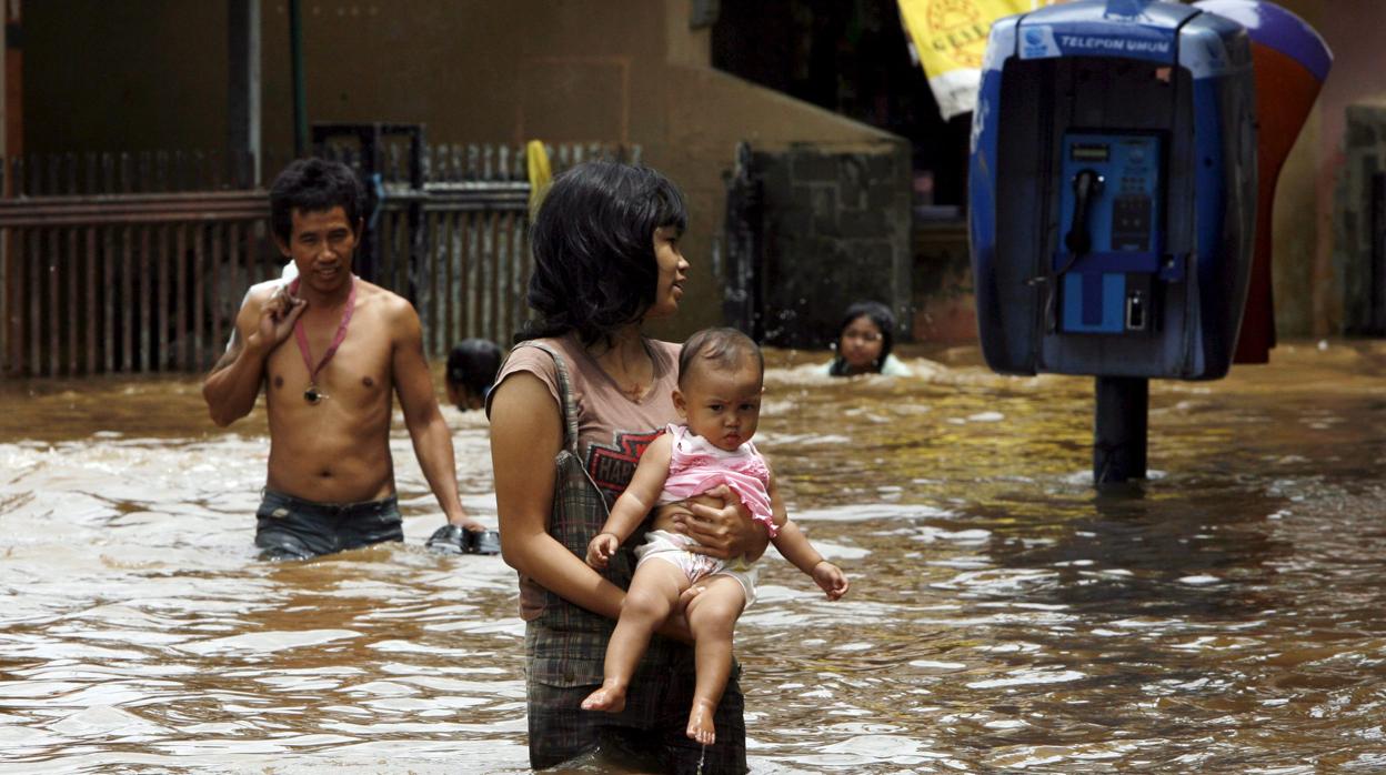 Fotografía del 6 de febrero de 2018, de varios residentes que caminan por una calle inundada por las aguas del río Ciliwung en Yakarta (Indonesia). Según informes oficiales, la parte noroeste de Yakarta se hunde a una velocidad de entre siete y 10 centímetros por año, lo que la convierte en una de las ciudades de más rápido hundimiento del mundo