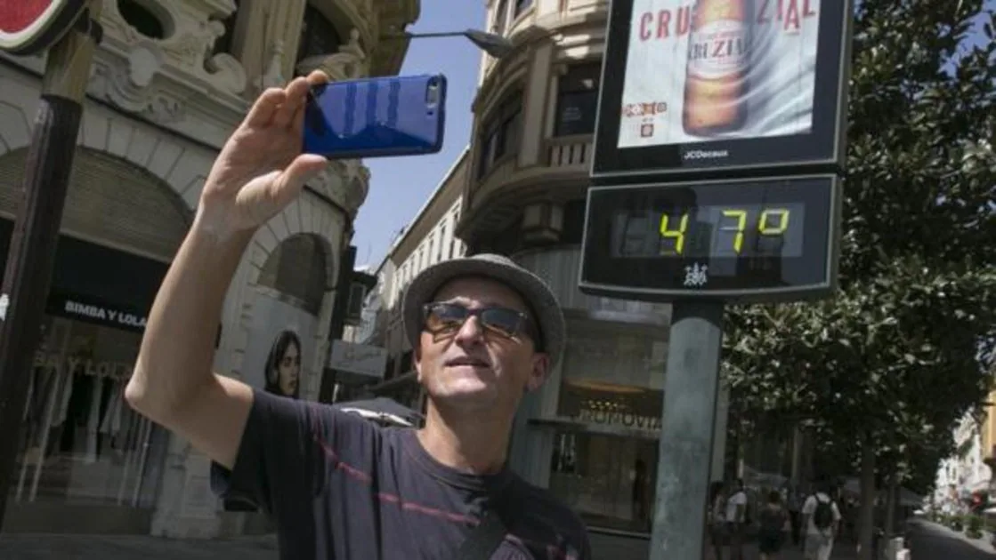 Un hombre se hace un selfie junto a un termómetro urbano