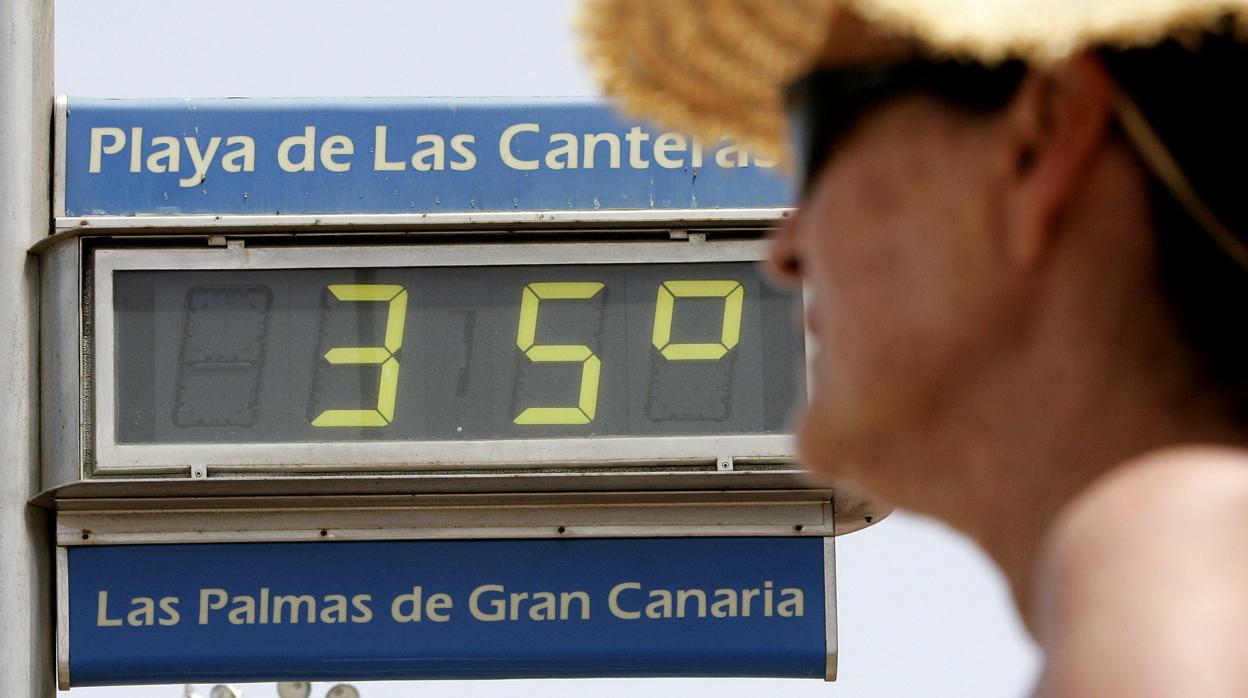 Una mujer se protege del calor junto a uno de los termómetros de la playa de Gran Canaria