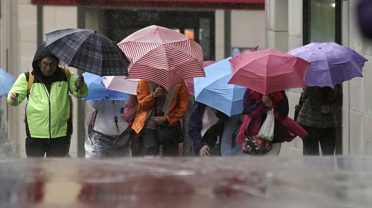 Varios peatones se protegen de la lluvia y viento, estos días en Tokio