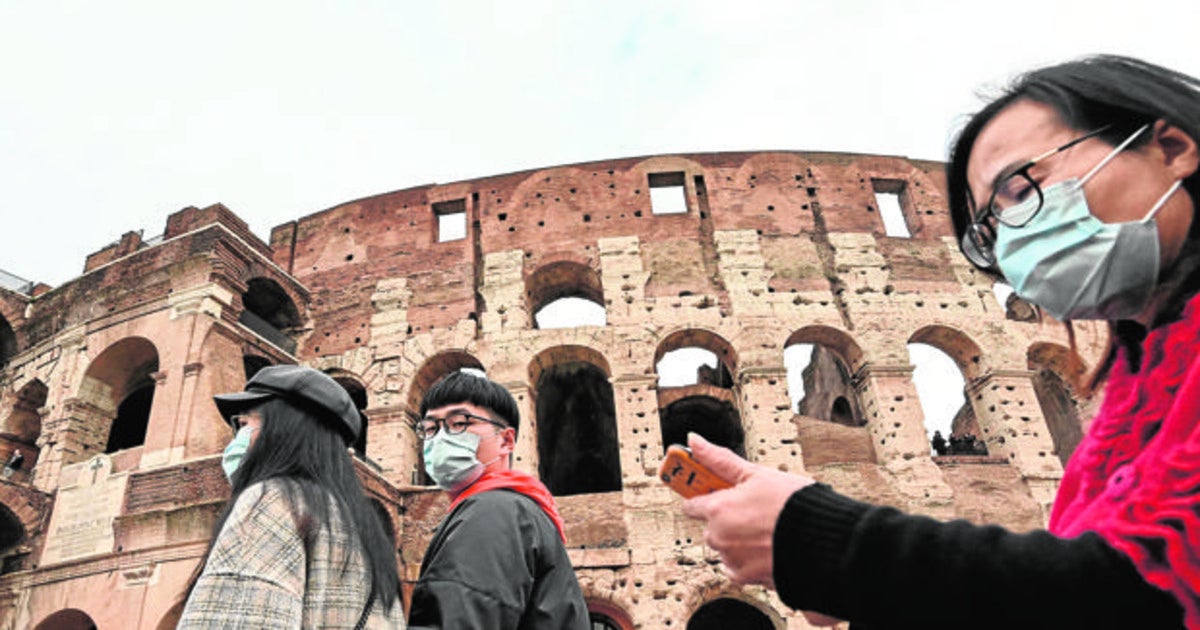 Unos turistas pasean con mascarillas frente al coliseo en Roma